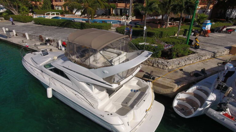 Aerial drone view of 42 ft Sea Ray flybridge yacht charter docked at Puerto Aventuras marina, Riviera Maya, with turquoise water alongside a catamaran
