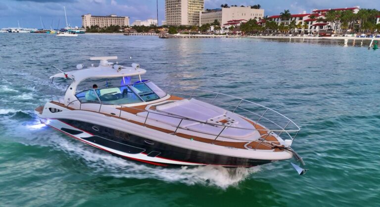 45 ft Sea Ray 455 Sundancer Atenea luxury yacht charter running at speed near Cancun marina at dusk with glowing blue underwater lights and hotel zone visible
