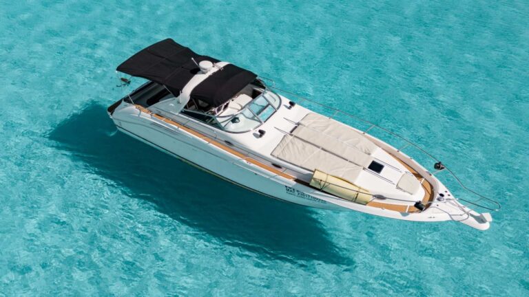 Aerial drone view of 45 ft Sea Ray Mavie luxury motor yacht charter anchored in shallow turquoise Caribbean water near Cancun, black bimini top and teak deck visible from above