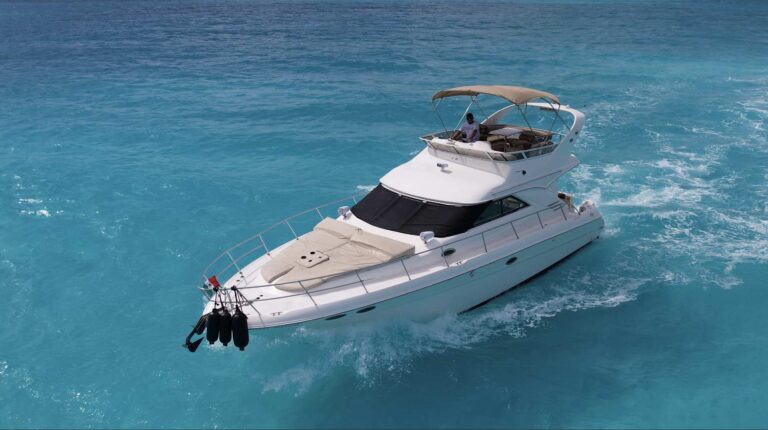 Aerial view of 45 ft Sea Ray flybridge Flycatcher luxury yacht charter running at speed across turquoise Caribbean water near Cancun, captain on upper flybridge helm station