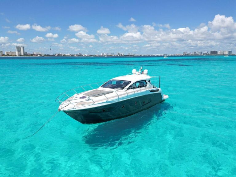 50 ft Azimut Volare luxury sport yacht charter anchored in brilliant turquoise Caribbean water with Cancun hotel zone skyline in background