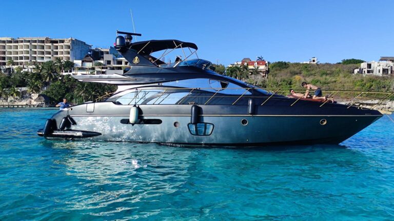 Starboard dockside view of the all-black 55 ft Azimut Kraken yacht at Puerto Cancun marina, two guests posing on upper deck with gold accent trim and Azimut branding visible