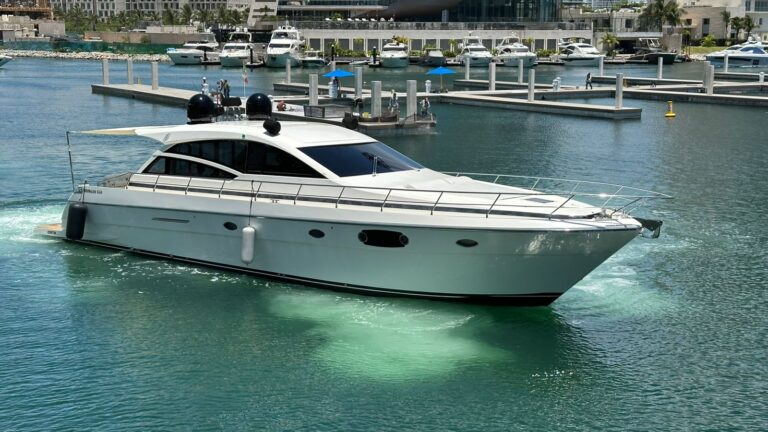 Port side exterior view of 55 ft Uniesse Yacht Perpetual luxury charter departing Playa Mujeres marina, sleek white hull with dark tinted windows navigating calm turquoise waters