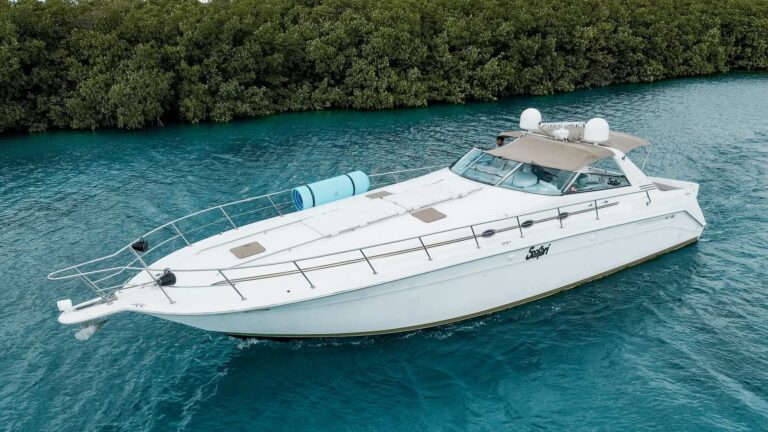 Aerial side view of 50 ft Sea Ray Seafari luxury yacht cruising through turquoise mangrove channel near Cancun, white hull, bimini canopy, teal floating mat on deck.
